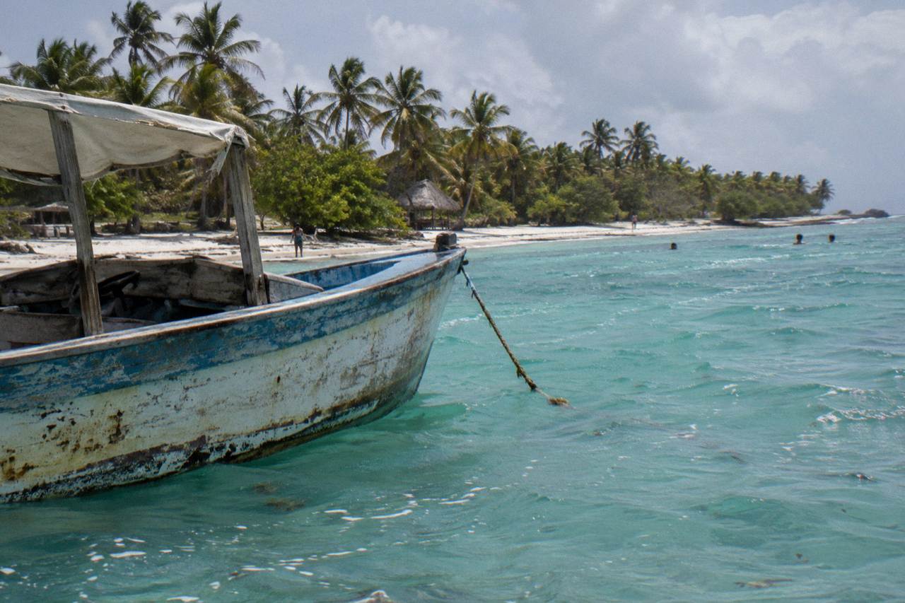 Wooden speedboat anchored in shallow turquoise water beside a palm-lined Caribbean beach