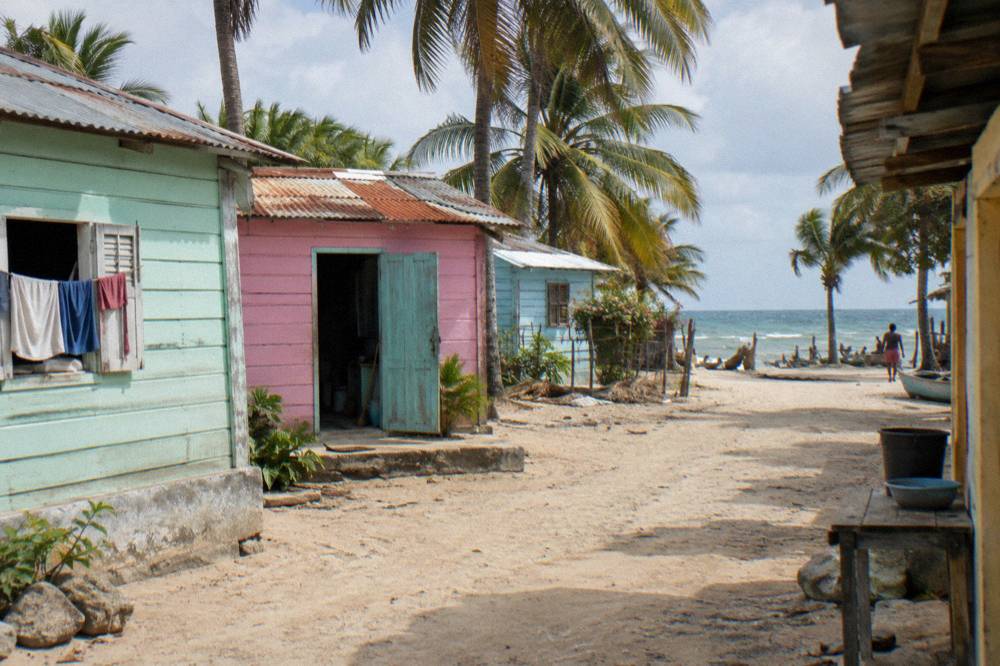 A small coastal village street with pastel painted buildings and palm trees in late afternoon light