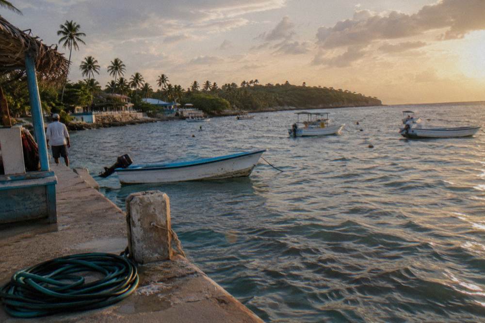 A calm Caribbean bay at golden hour with anchored boats and a distant tree covered island