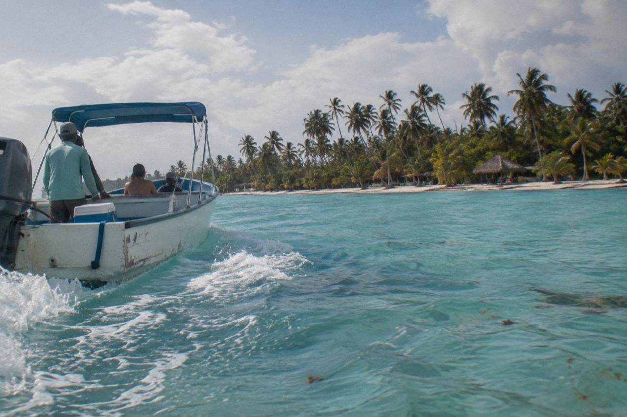 A speedboat cutting across calm turquoise Caribbean water toward a palm lined island shoreline