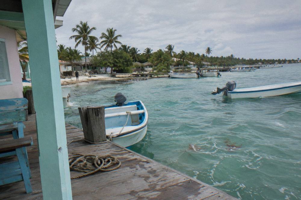 Small boats moored in clear turquoise water at a Caribbean village pier in morning light