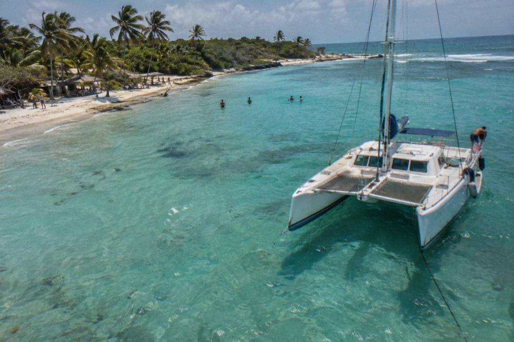 A white catamaran anchored in clear turquoise water near a sandy beach
