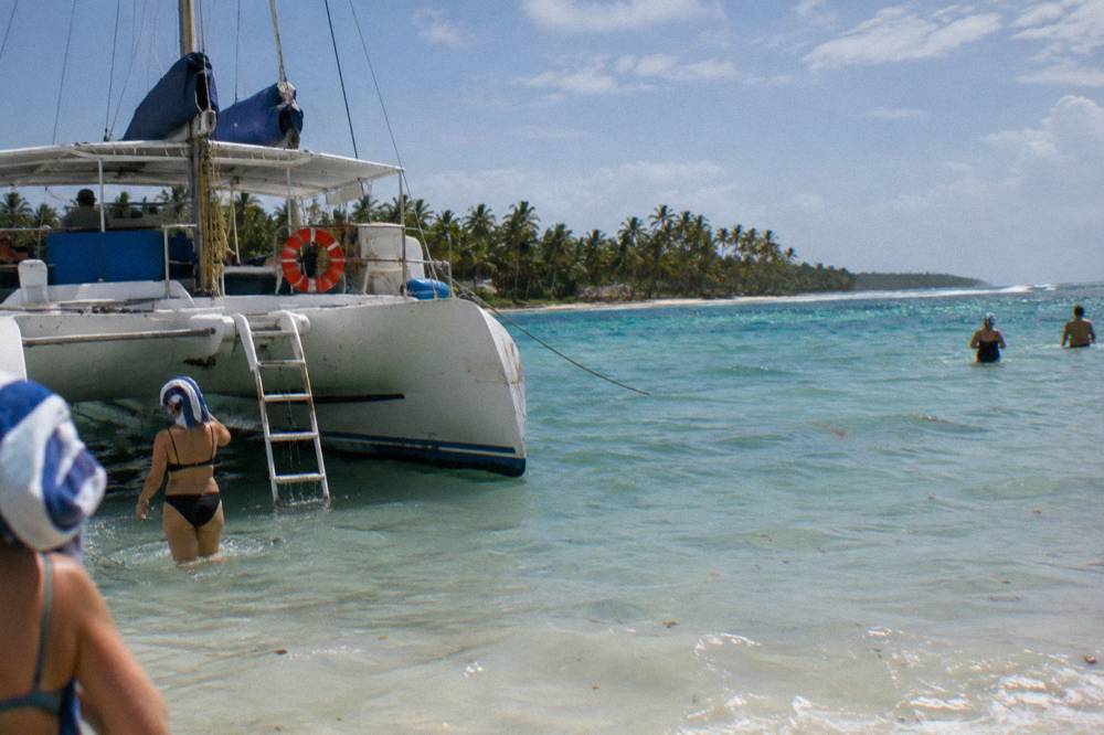 Catamaran anchored in shallow turquoise water with guests wading nearby