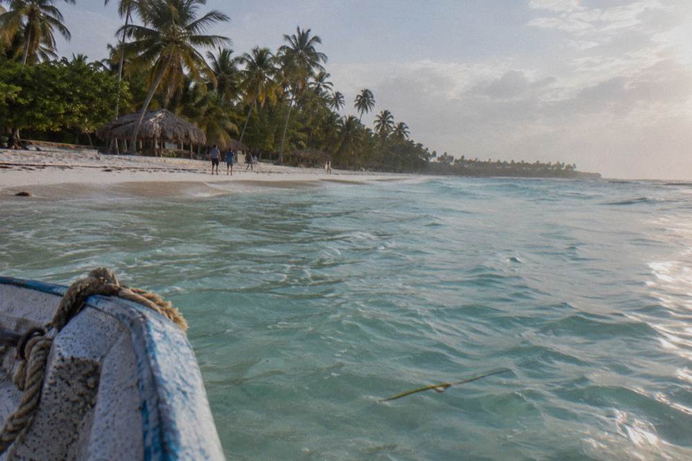 Calm shallow turquoise water over a sandbar with distant palm-lined shoreline