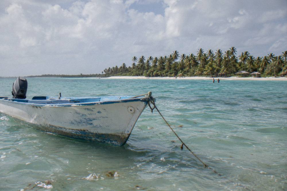 Speedboat anchored in shallow turquoise water near a sandbar with distant palm island