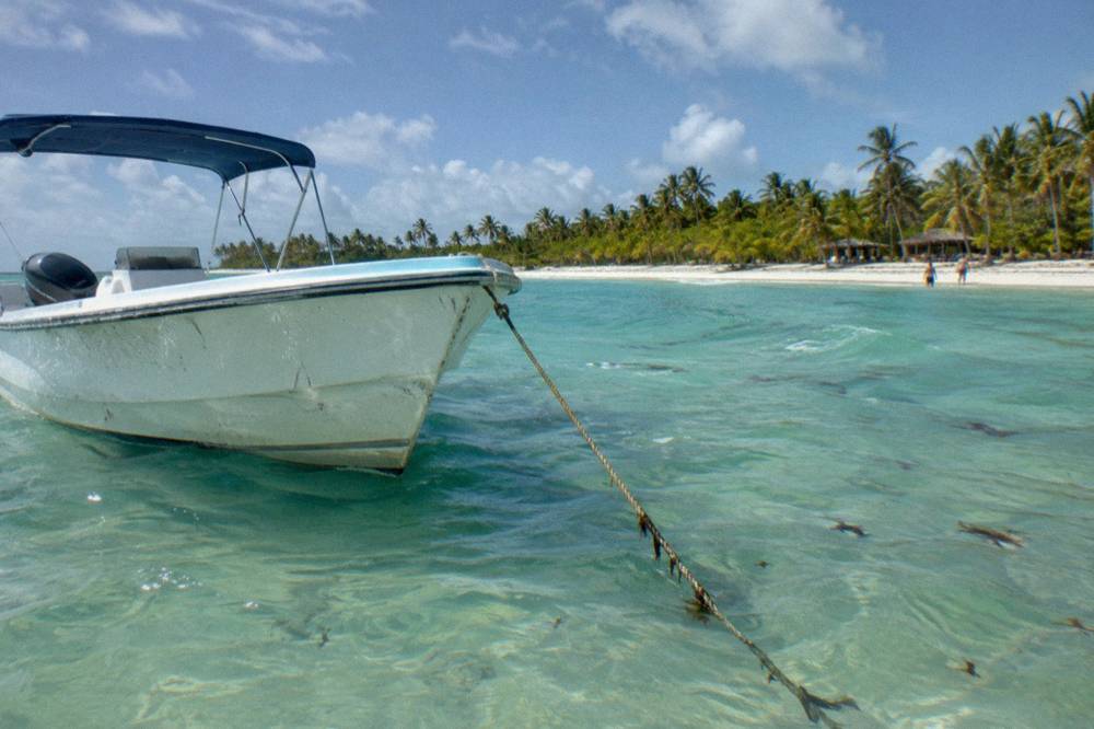 A white speedboat anchored in clear shallow turquoise water near a sandbar