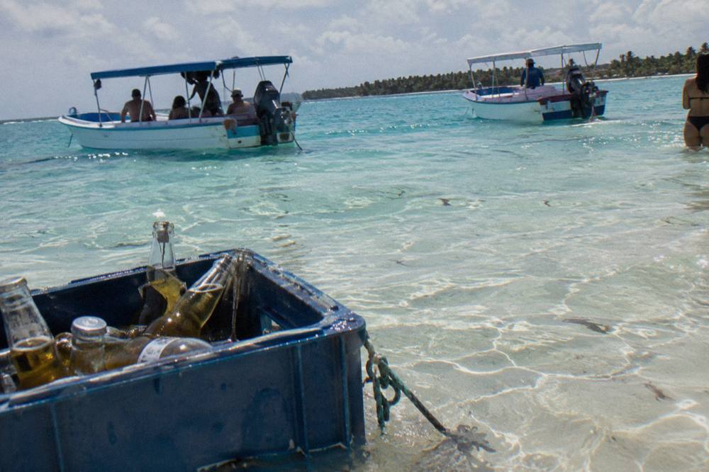 Shallow turquoise sandbar in open sea with a few boats anchored nearby