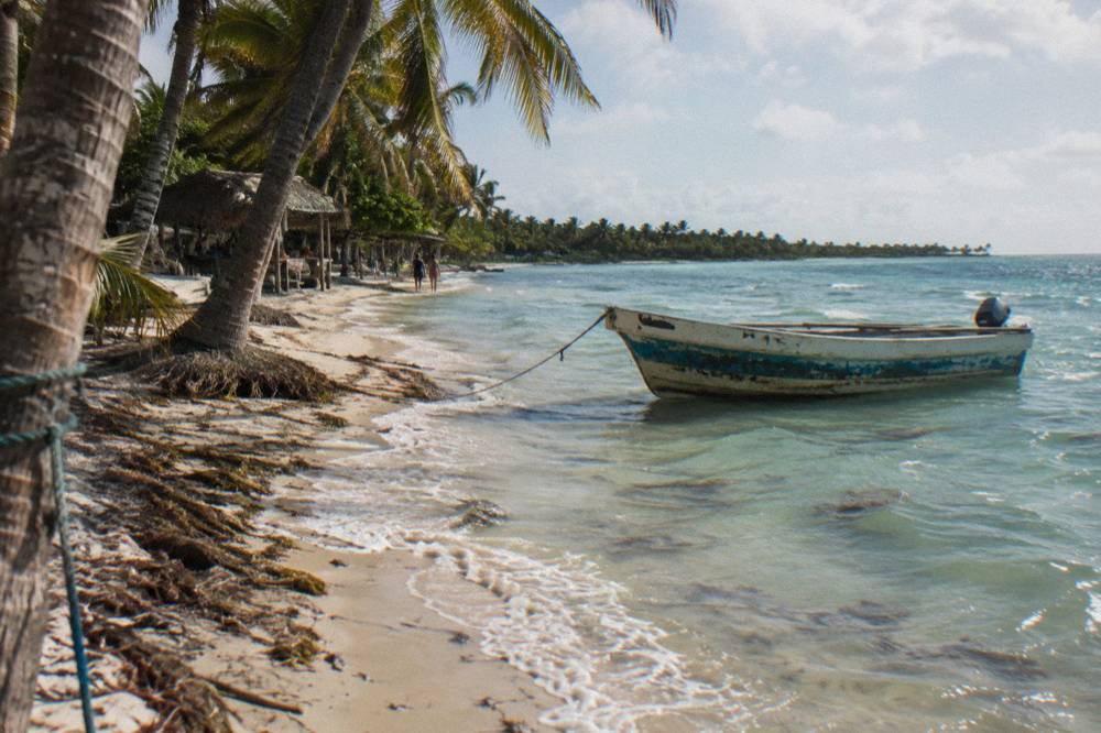 Palm trees along a pale sand beach with clear shallow water and a wooden boat at anchor