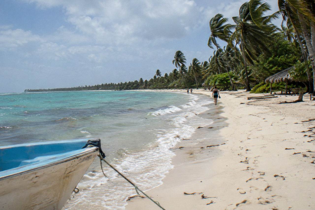 Wide Caribbean beach with pale sand, turquoise shallows and a line of palm trees along the shore