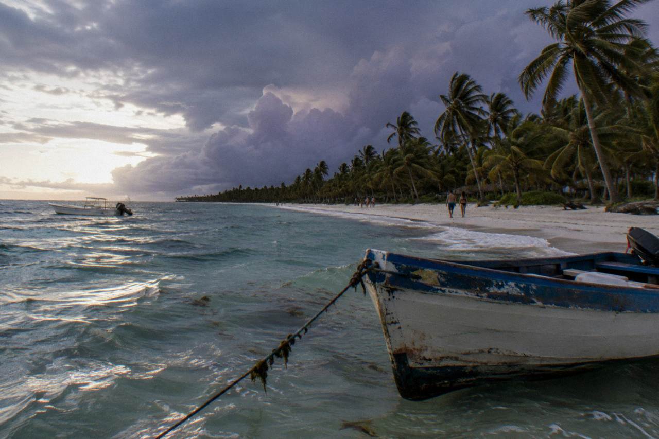 A wooden boat anchored off a white sand beach with tall palm trees along the shoreline