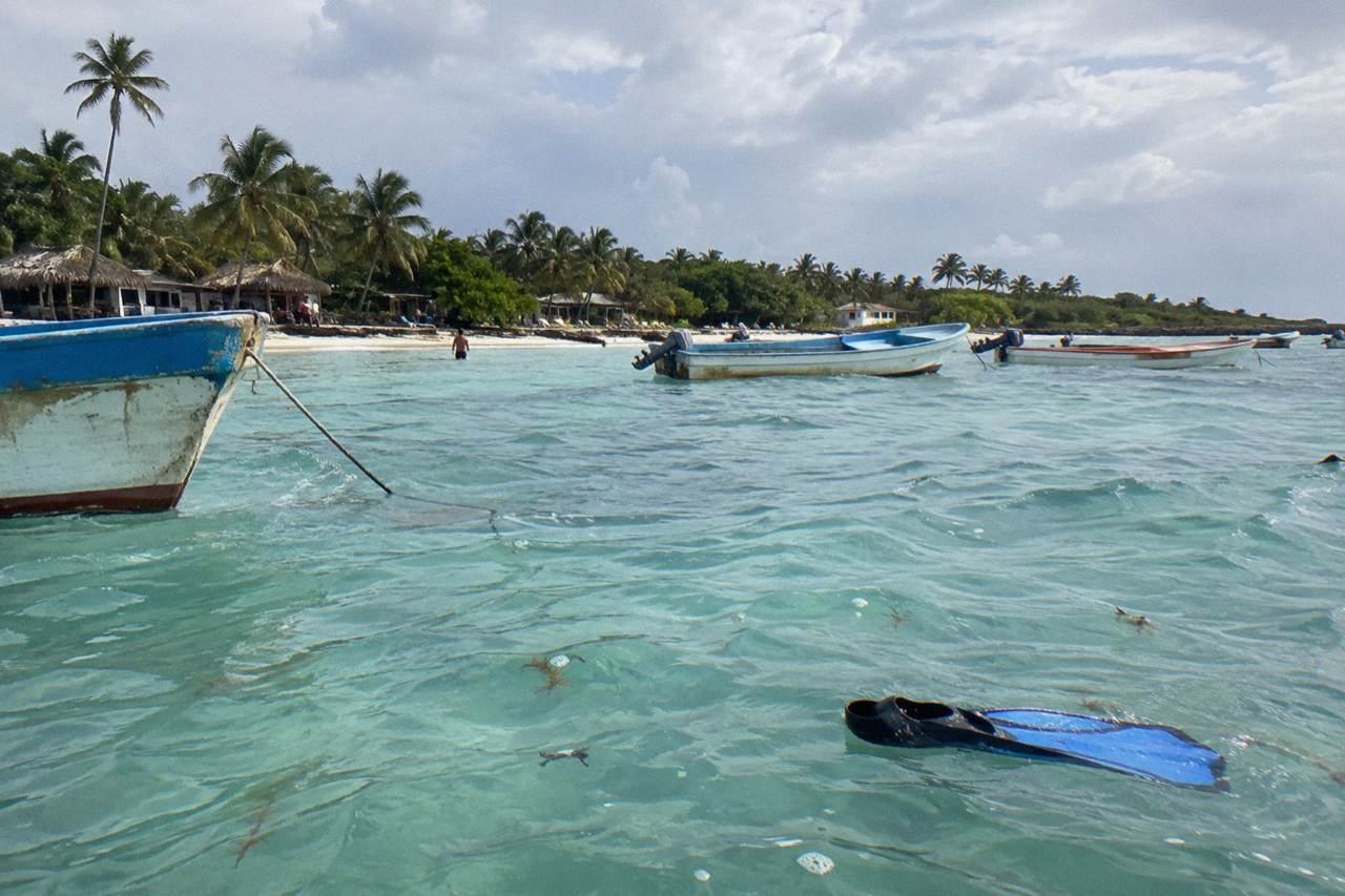 Calm turquoise water over sand at a small Caribbean fishing village beach with palm trees and moored boats