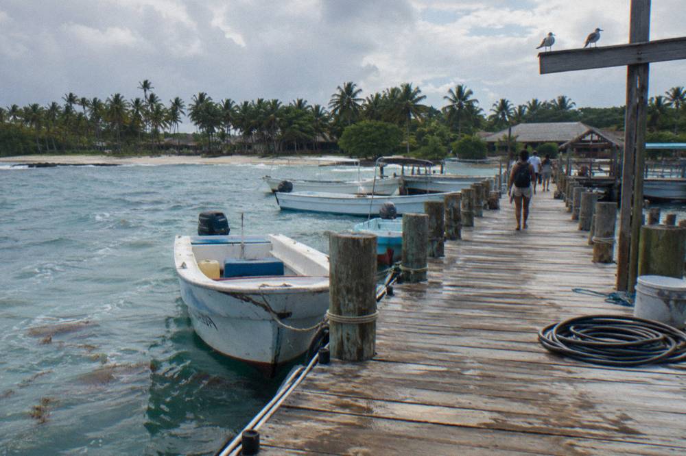 A wooden pier extending into calm green sea with small boats tied alongside
