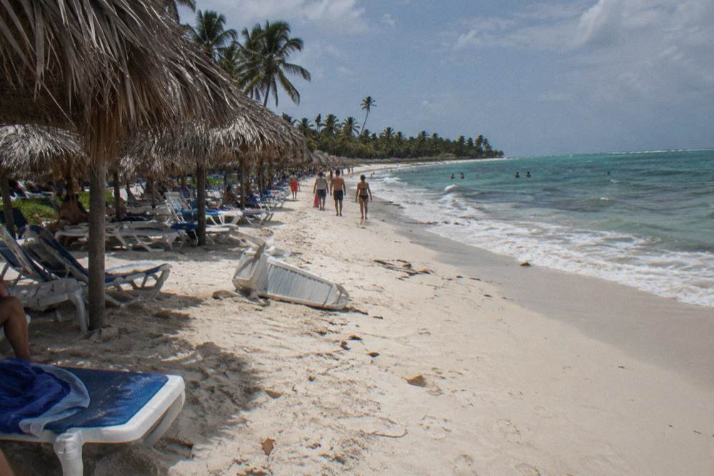 A wide sandy beach lined with thatched palm umbrellas and rows of loungers under clear sky