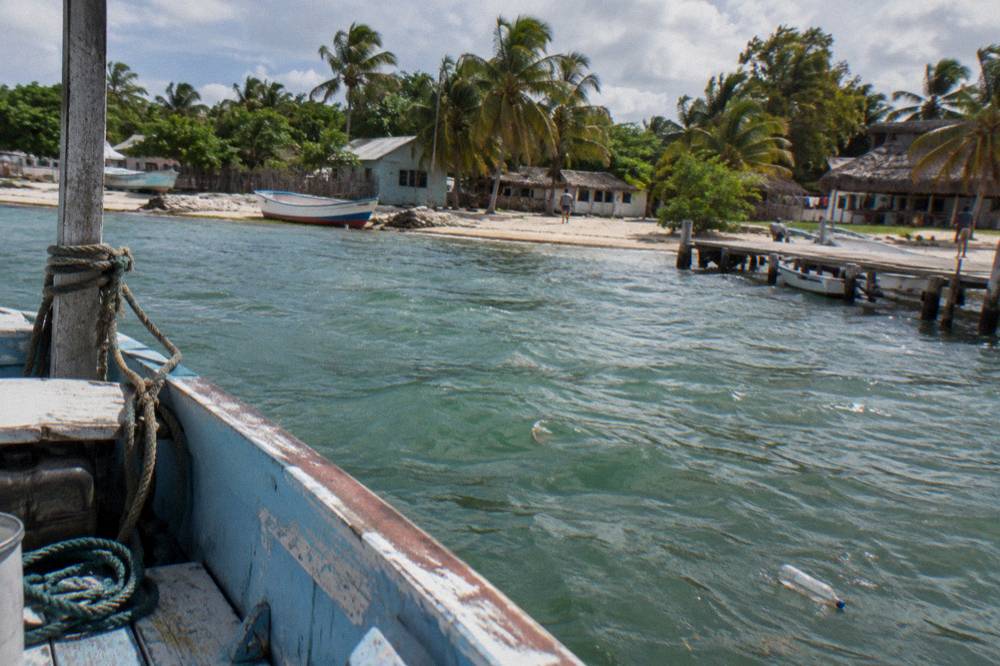 Weathered fishing boats moored in a small harbor beside calm green water under a partly cloudy sky