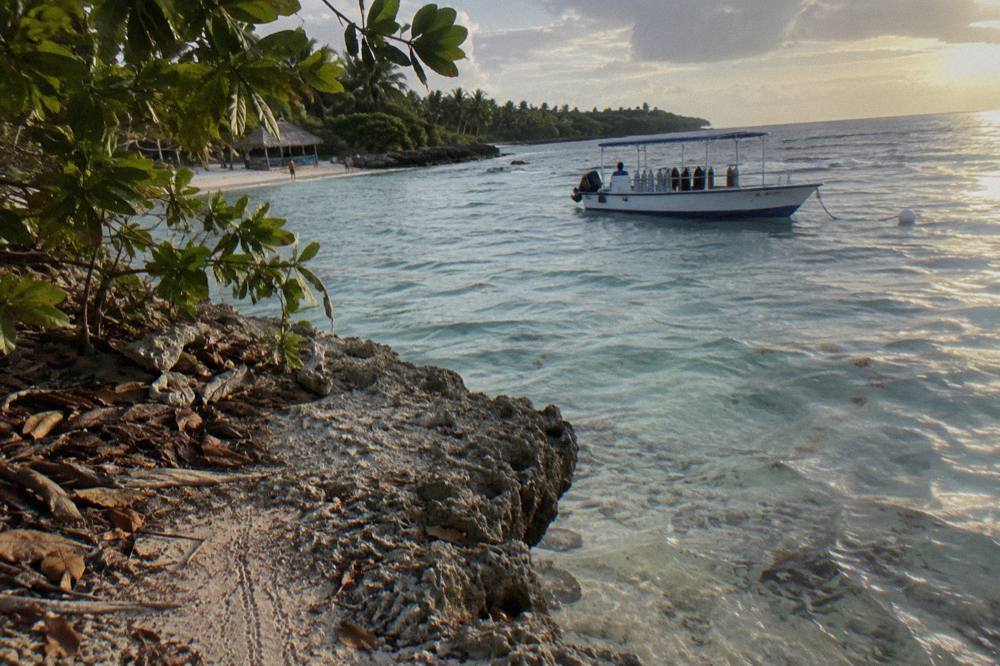 Wooded island shoreline with clear shallow water and a moored dive boat