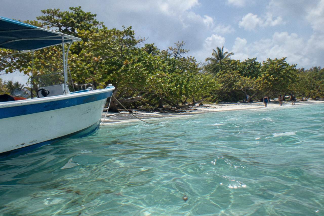 Small boat anchored over turquoise shallows beside a wooded Caribbean island