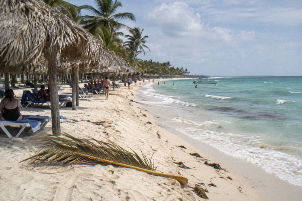 Wide sandy beach with turquoise water and a line of thatched shade palapas