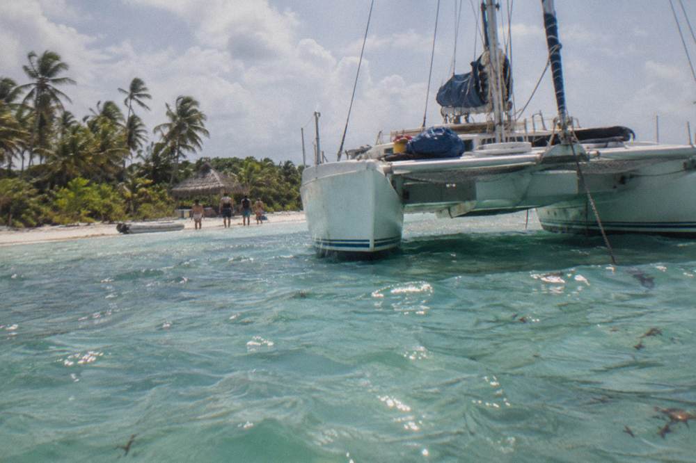 White catamaran anchored in shallow turquoise water beside a sandbar