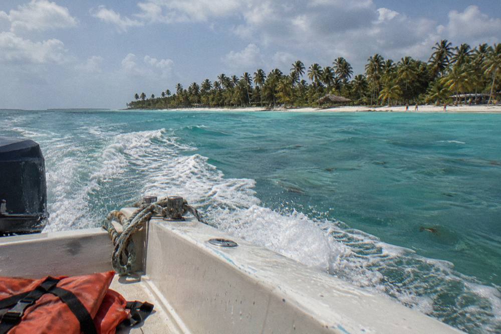 Speedboat cruising over calm turquoise Caribbean water toward a palm-lined island beach