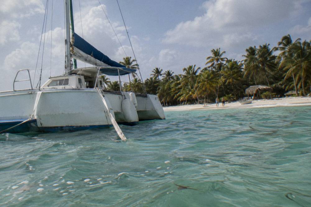 Catamaran anchored off a white sand beach with palm trees and clear shallow water