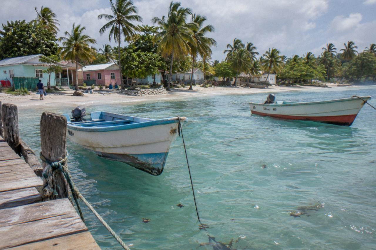 Wooden boats anchored in clear turquoise water beside a small Caribbean fishing village dock