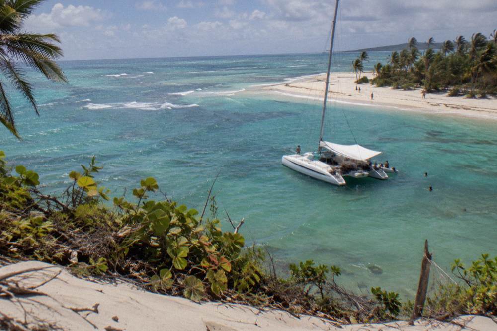 A catamaran anchored over shallow turquoise water near a sandbar