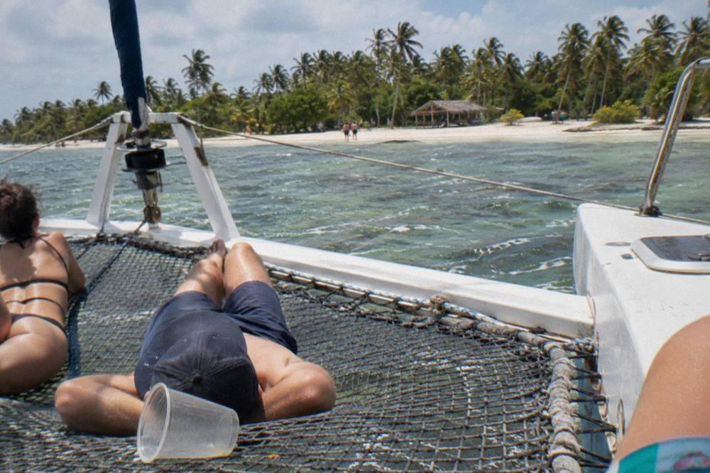 Passengers lounging on the netting of a catamaran in clear shallow water