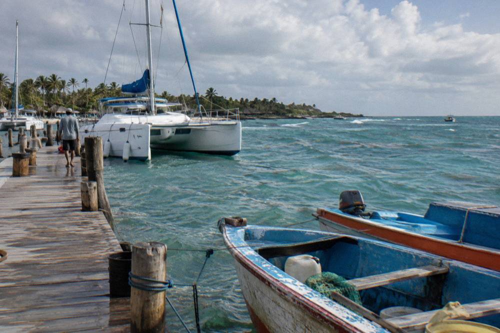A wooden pier at Bayahibe with catamarans moored beside fishing boats in the morning