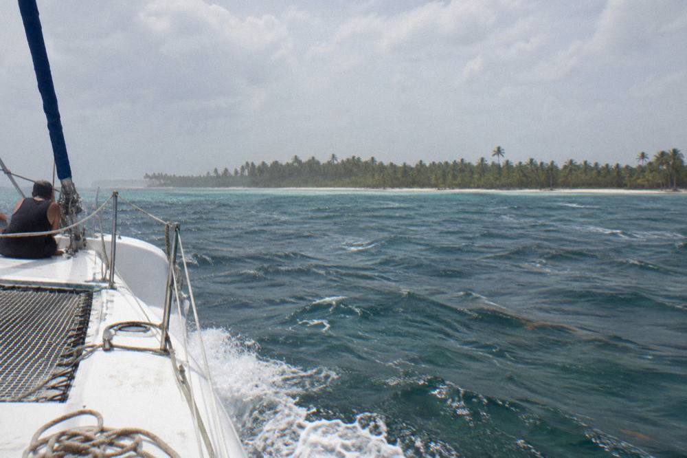 A catamaran under way on calm Caribbean water with palm coastline in the distance
