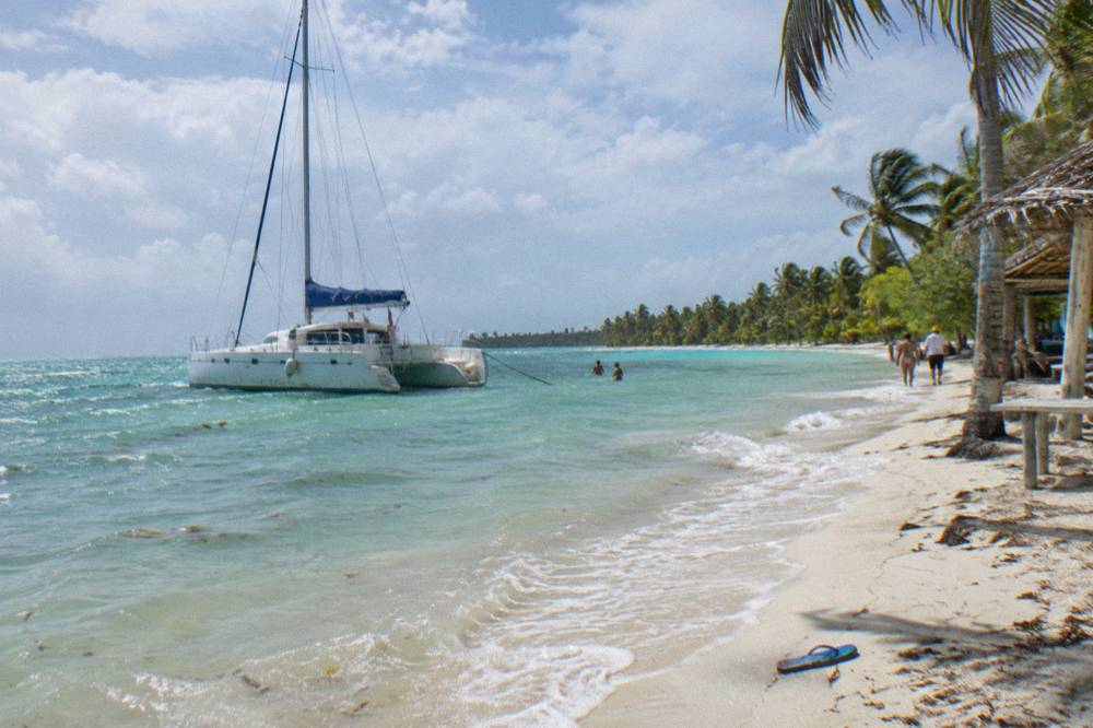 Catamaran anchored in shallow turquoise water near a wide sand beach