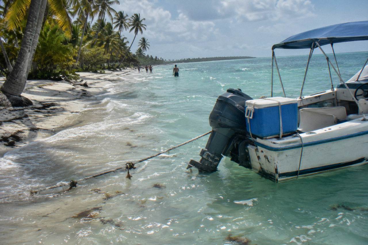 Speedboat anchored in shallow turquoise water beside a palm lined white sand beach