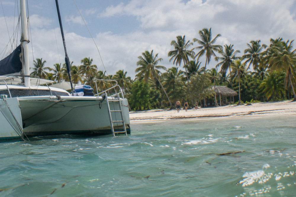 Catamaran anchored off a wide white sand beach lined with palm trees on Saona Island