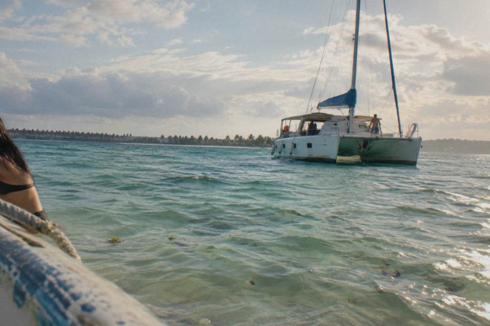 A sleek white catamaran anchored in shallow turquoise water near a sandbar with distant palm island silhouette