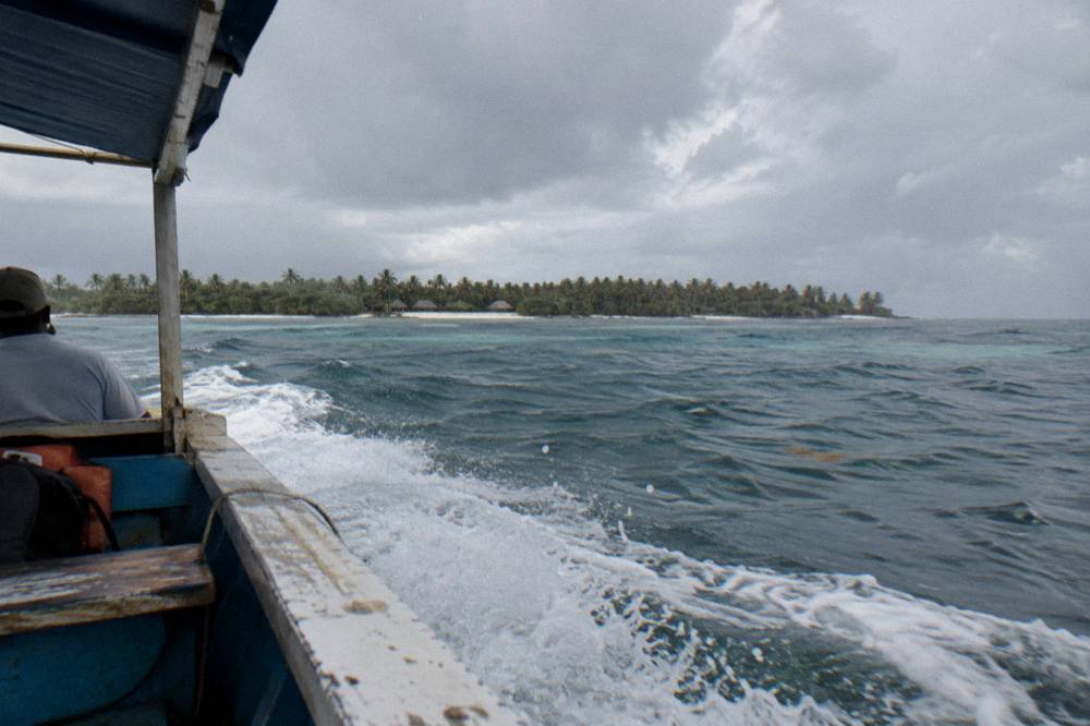 A wooden speedboat crossing open Caribbean water toward a low green island on the horizon
