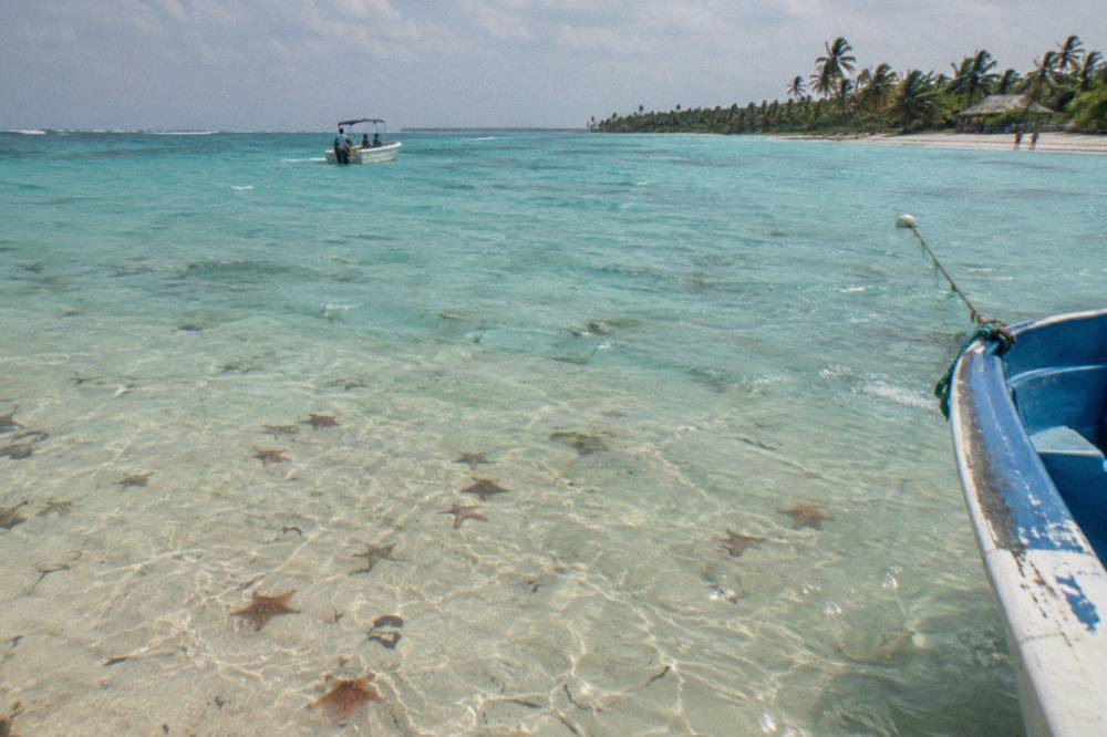 Turquoise shallow sandbar with scattered starfish on the sandy bottom and a moored boat in the distance