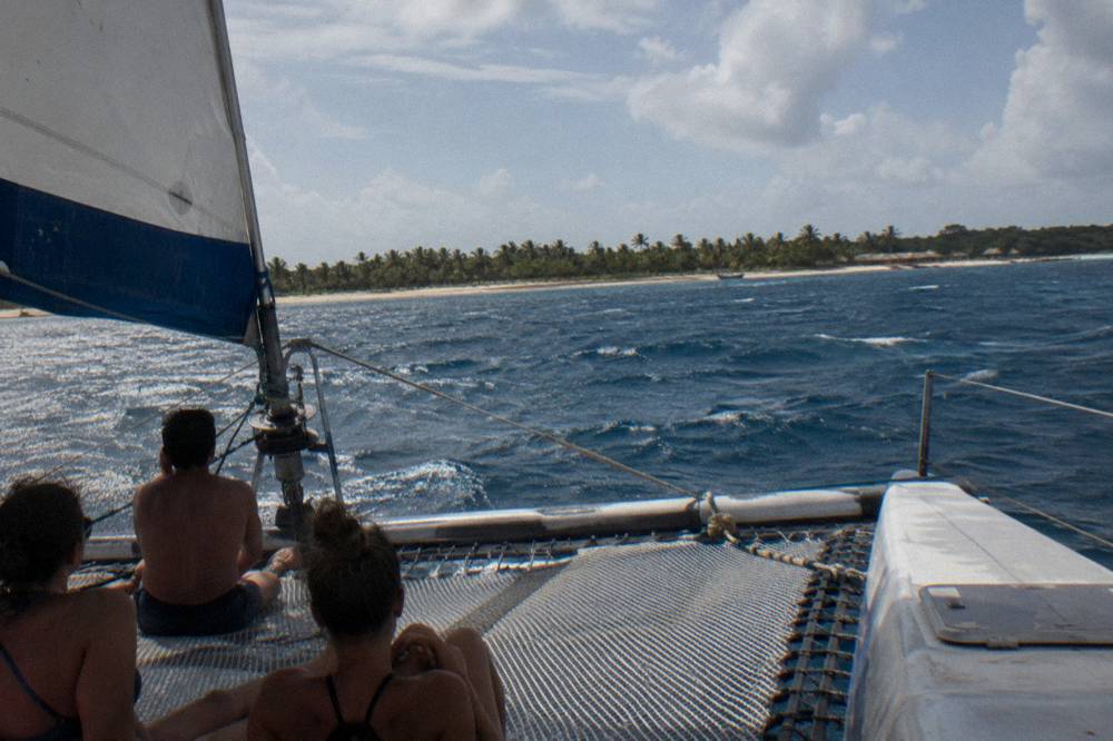 Catamaran under sail on open Caribbean water at midday with passengers on the net at the bow
