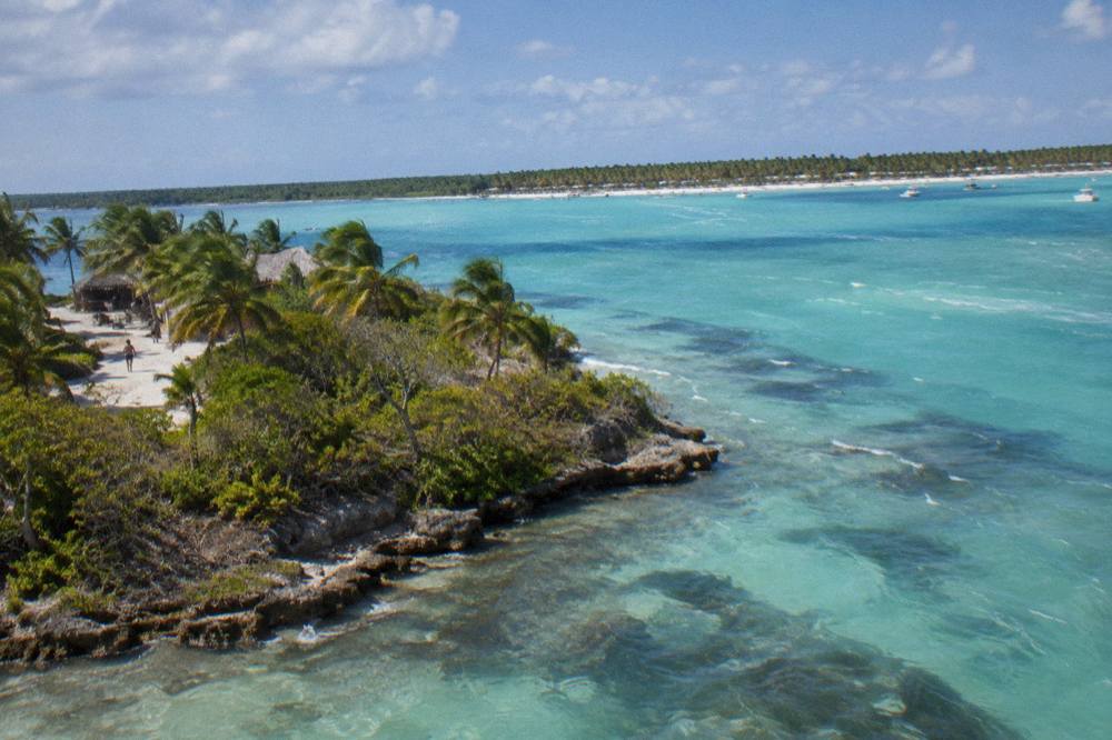 Aerial view of a turquoise channel between a palm covered islet and a long white sand beach