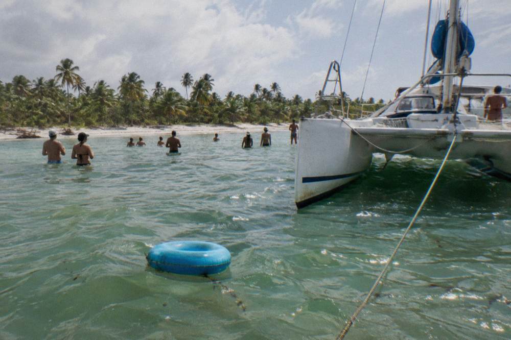 Catamaran anchored in shallow clear water with guests standing in the sea