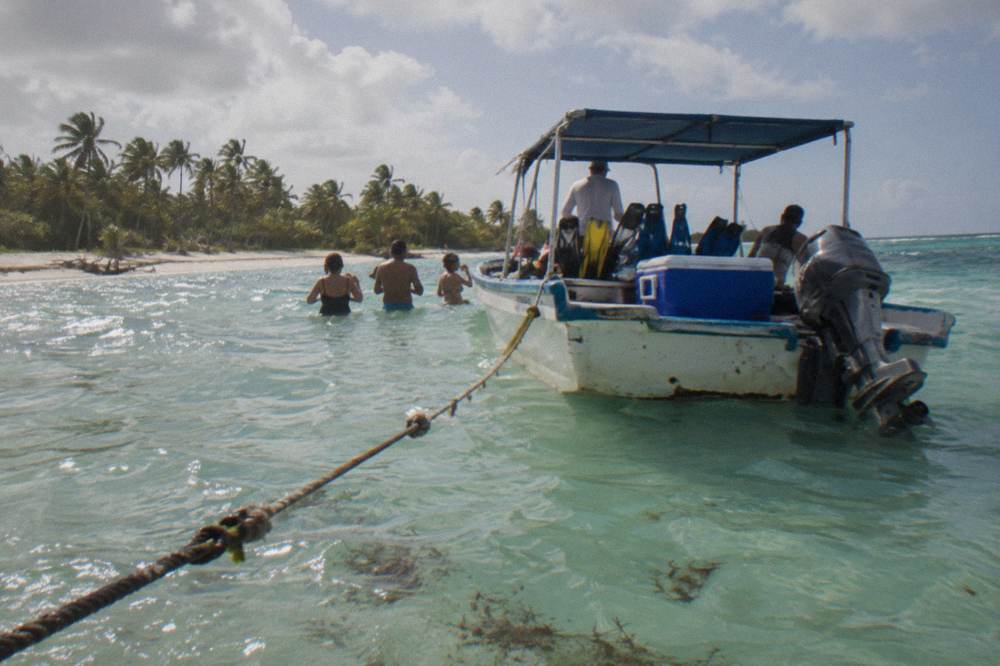 Snorkel boat anchored over a shallow sandbar with passengers standing in clear water