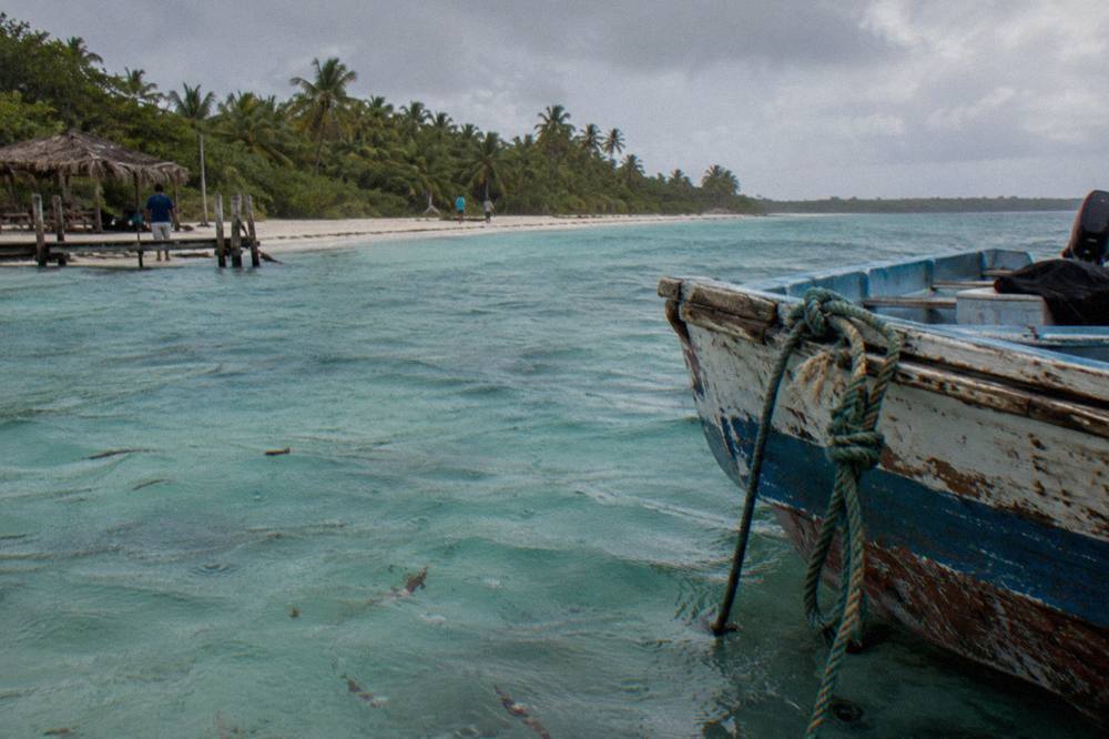A wooden fishing boat anchored in shallow turquoise water near a Saona beach