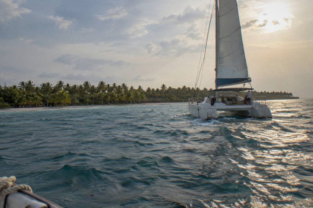 A catamaran with passengers sailing on calm Caribbean water toward Saona