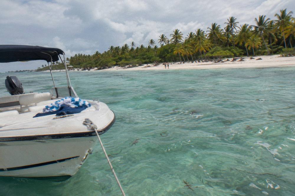 An empty private speedboat moored in shallow turquoise water beside a sandbar at the Saona natural pool
