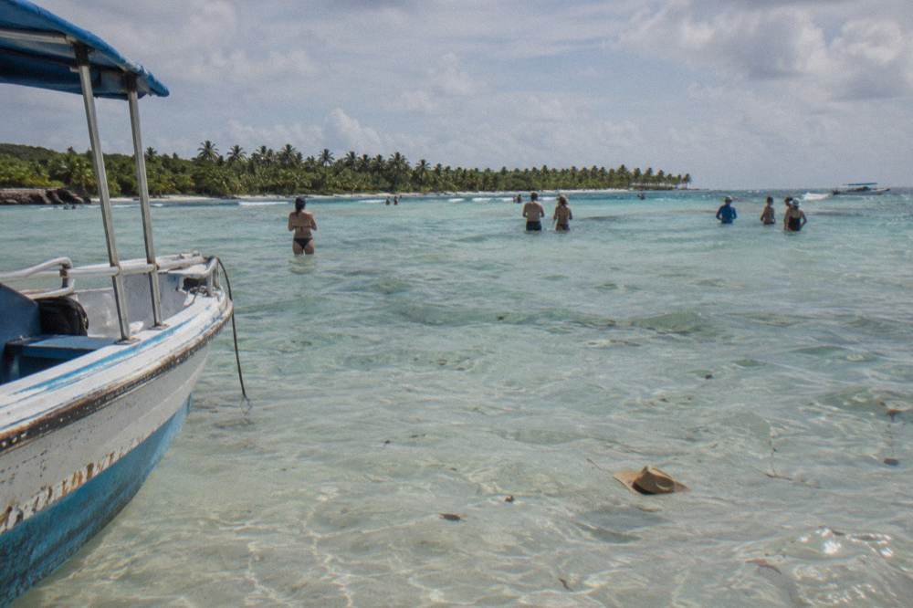 Wading guests standing in waist-deep clear water on a sandbar at the Saona natural pool