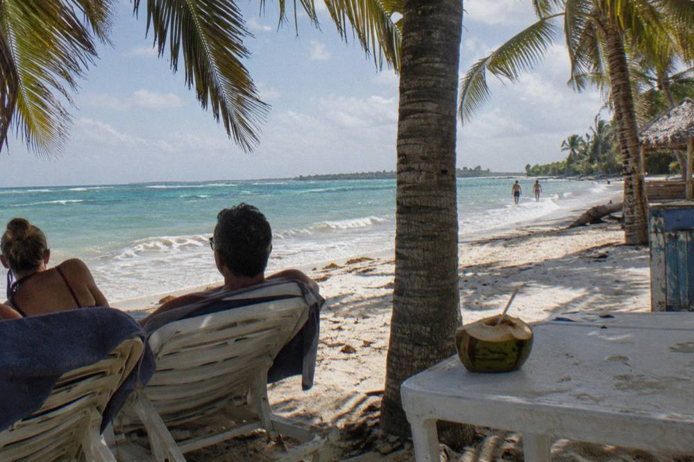 A couple sharing a shaded lounge area on a near-empty white sand beach on Saona Island