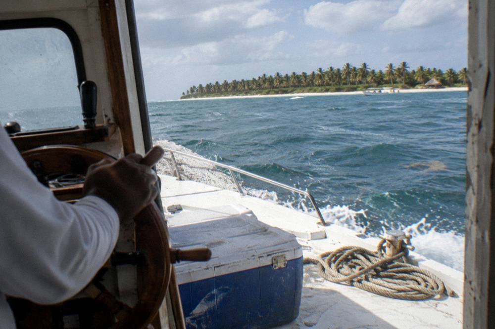A boat captain at the wheel of a small private tour boat heading across open Caribbean water