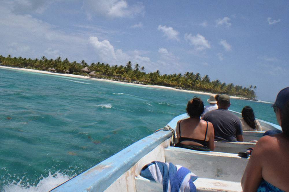 Passengers seated on the bow of a boat crossing open turquoise Caribbean water