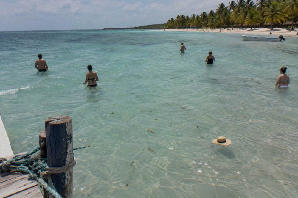 A wide shallow sandbar with bathers standing in clear water under a bright sky
