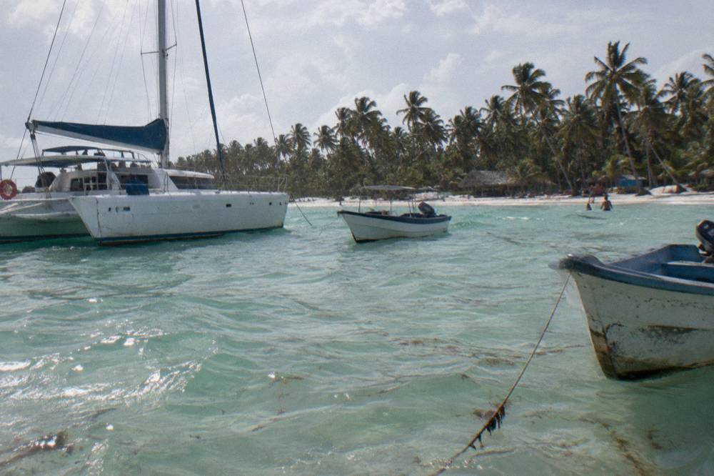 Anchored catamaran and moored boats in clear shallow water beside a white sand beach