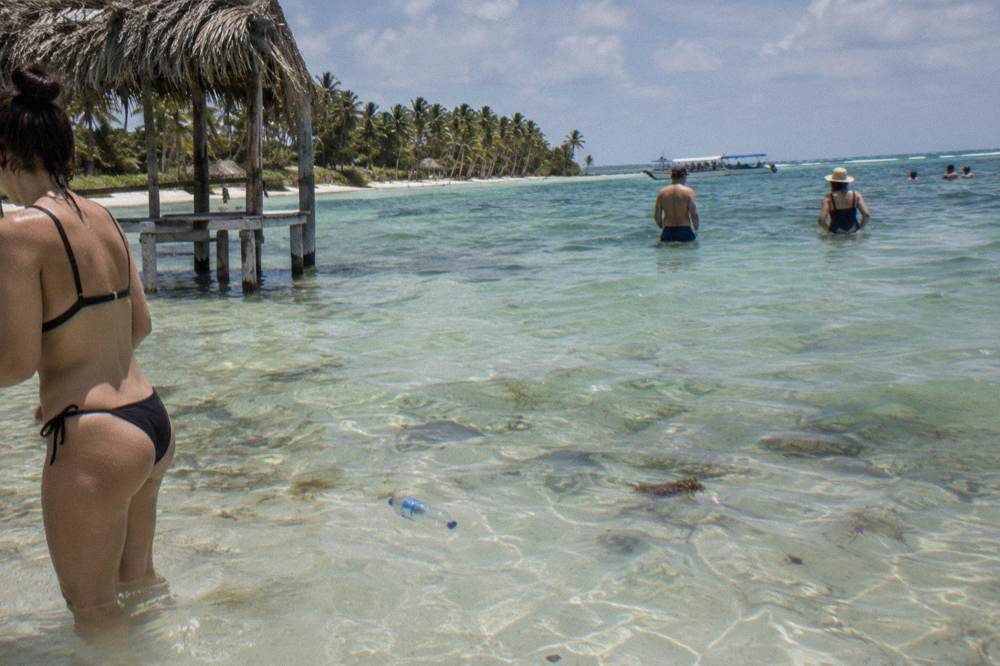Shallow turquoise natural pool sandbar with bathers standing in waist-deep clear water