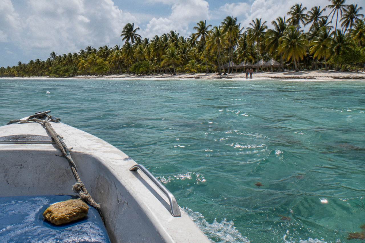 Open speedboat cutting across calm turquoise water toward a palm-lined Caribbean beach